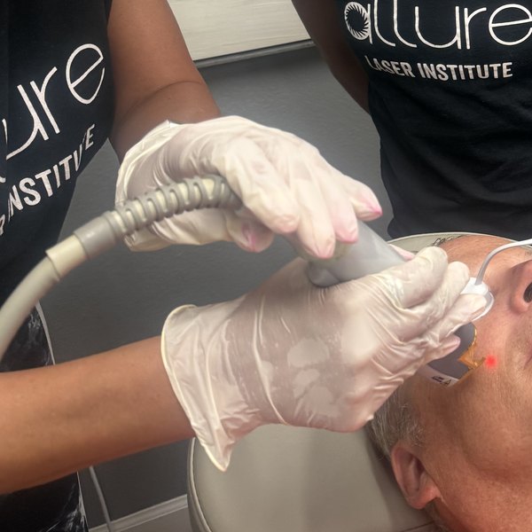 Gloved hands holding a laser handpiece to a model's cheek